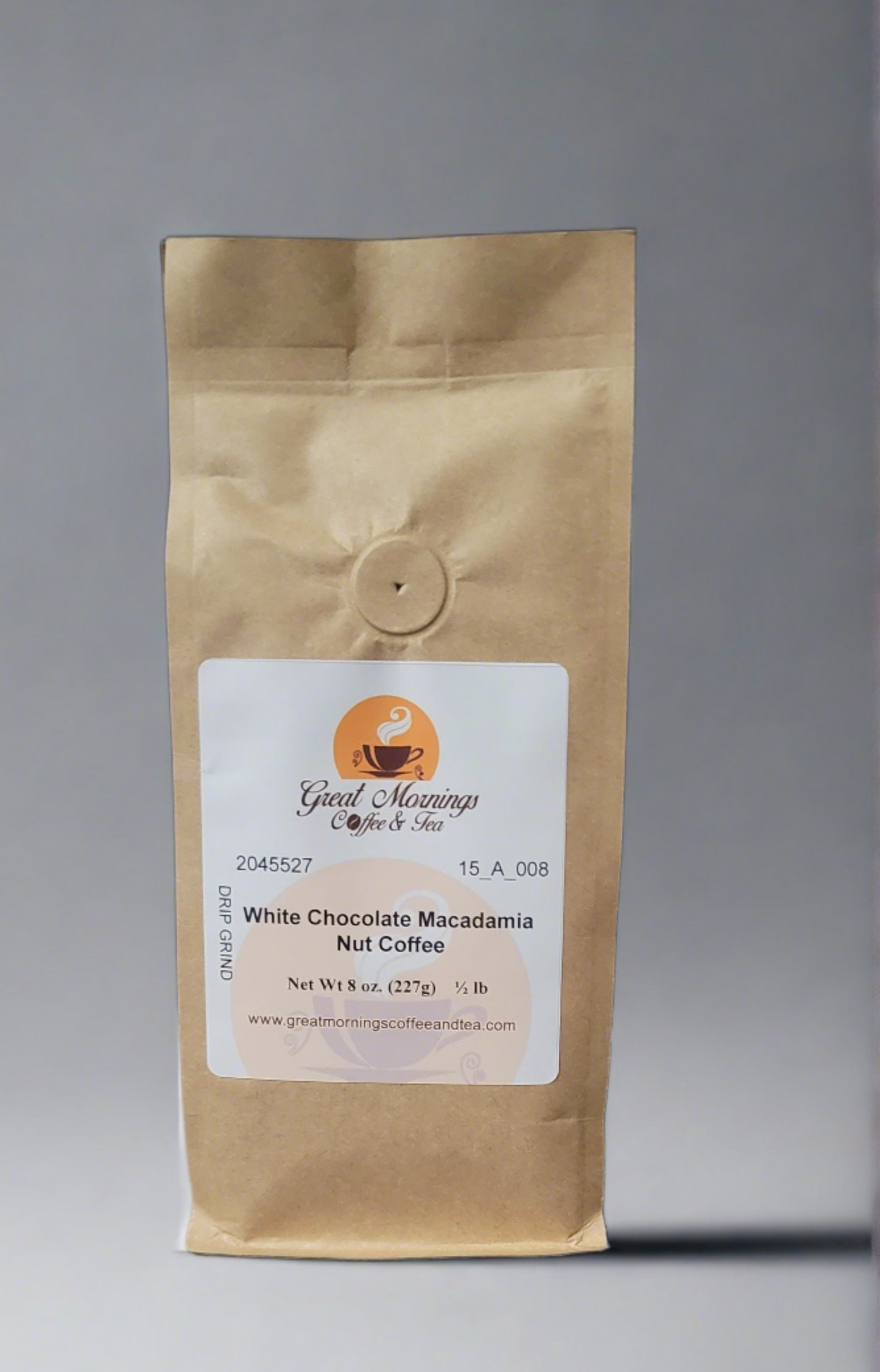 A photo of a vertical brown paper coffee bag on a gray background. The bag has a white label with the logo "Great Mornings Coffee & Tea," featuring a stylized orange coffee cup with steam. Text on the label includes a product code "2045527 15_A_008," the flavor "White Chocolate Macadamia Nut Coffee," and details "Net Wt 8 oz. (227g) ½ lb." Below is the website "www.greatmorningscoffeeandtea.com.