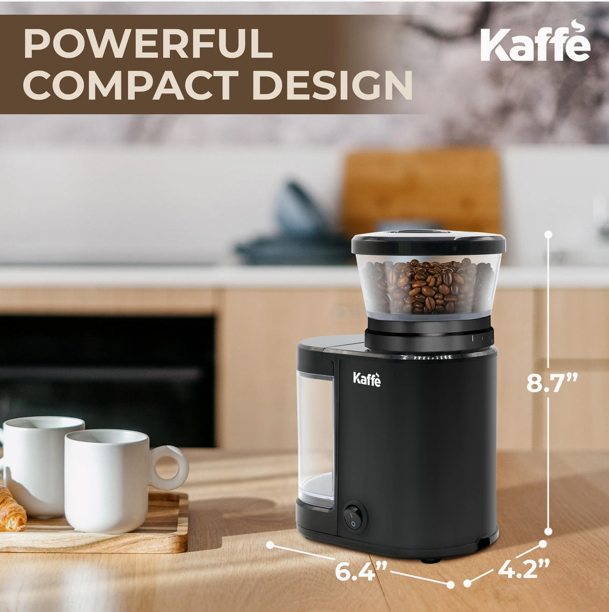 A compact black Kaffe coffee grinder with a clear bean hopper filled with coffee beans, shown on a wooden countertop in a blurred kitchen setting. White text at the top reads 'POWERFUL COMPACT DESIGN,' and dimension lines indicate 8.