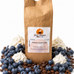 Great Mornings Blueberry Cream Coffee in a kraft paper bag on a white studio background, surrounded by fresh blueberries, dollops of whipped cream, and roasted coffee beans.