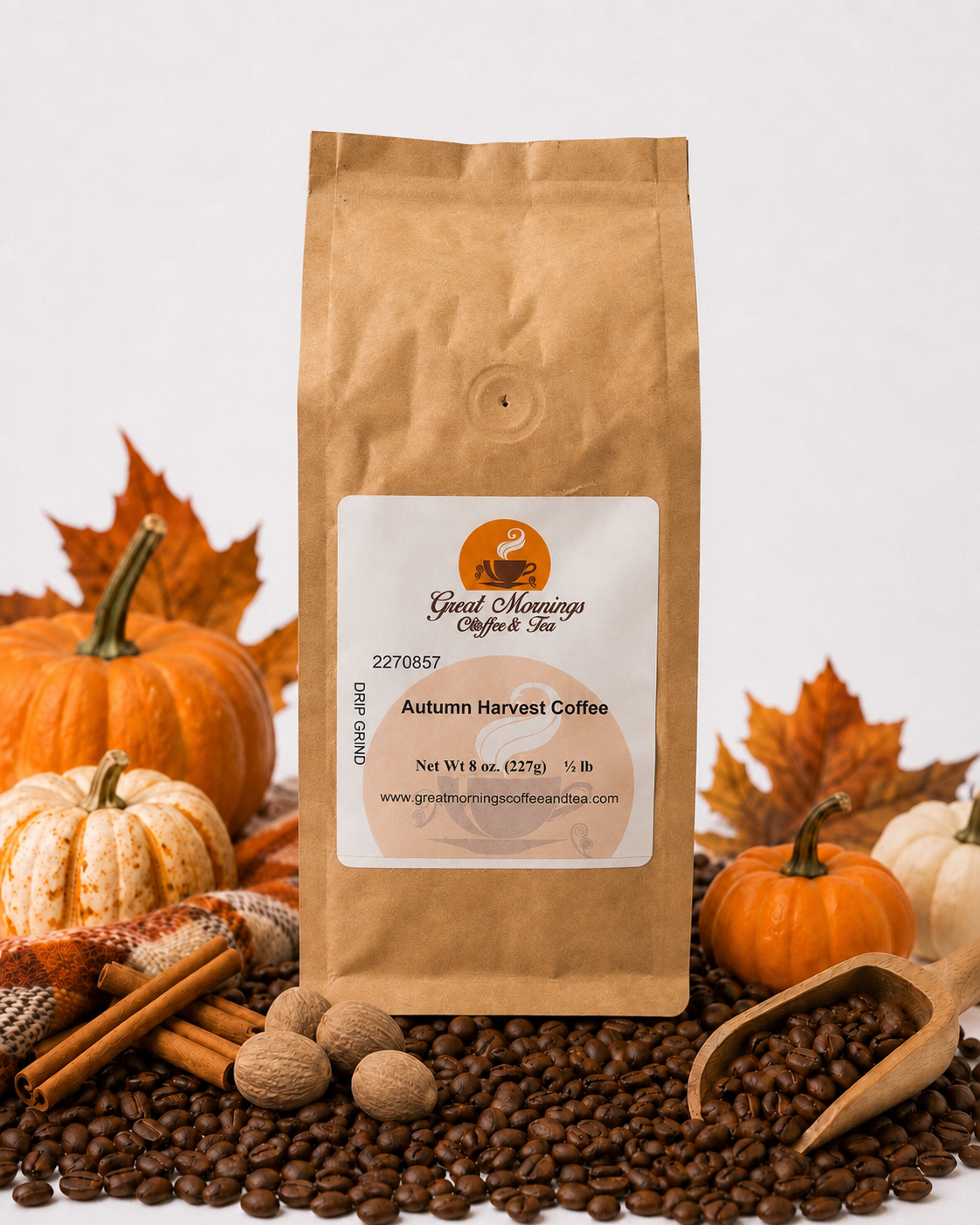 Great Mornings Autumn Harvest Coffee in a kraft paper bag on a white studio background, surrounded by roasted coffee beans, whole nutmeg, cinnamon sticks, small pumpkins, autumn leaves, and a warm plaid blanket.