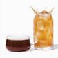 Glass of iced tea with a splash next to a cup of dark tea on a white background