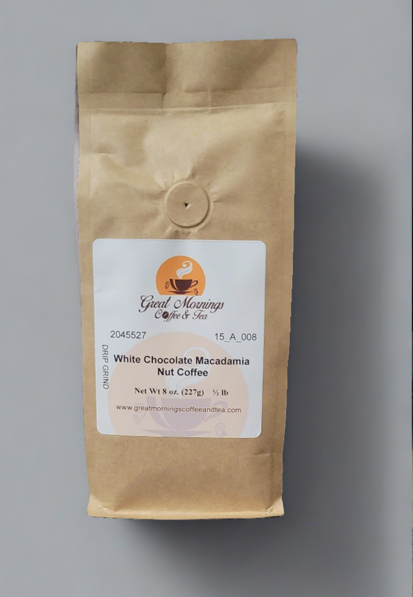 A photo of a vertical brown paper coffee bag on a gray background. The bag has a white label with the logo "Great Mornings Coffee & Tea," featuring a stylized orange coffee cup with steam. Text on the label includes a product code "2045527 15_A_008," the flavor "White Chocolate Macadamia Nut Coffee," and details "Net Wt 8 oz. (227g) ½ lb." Below is the website "www.greatmorningscoffeeandtea.com.